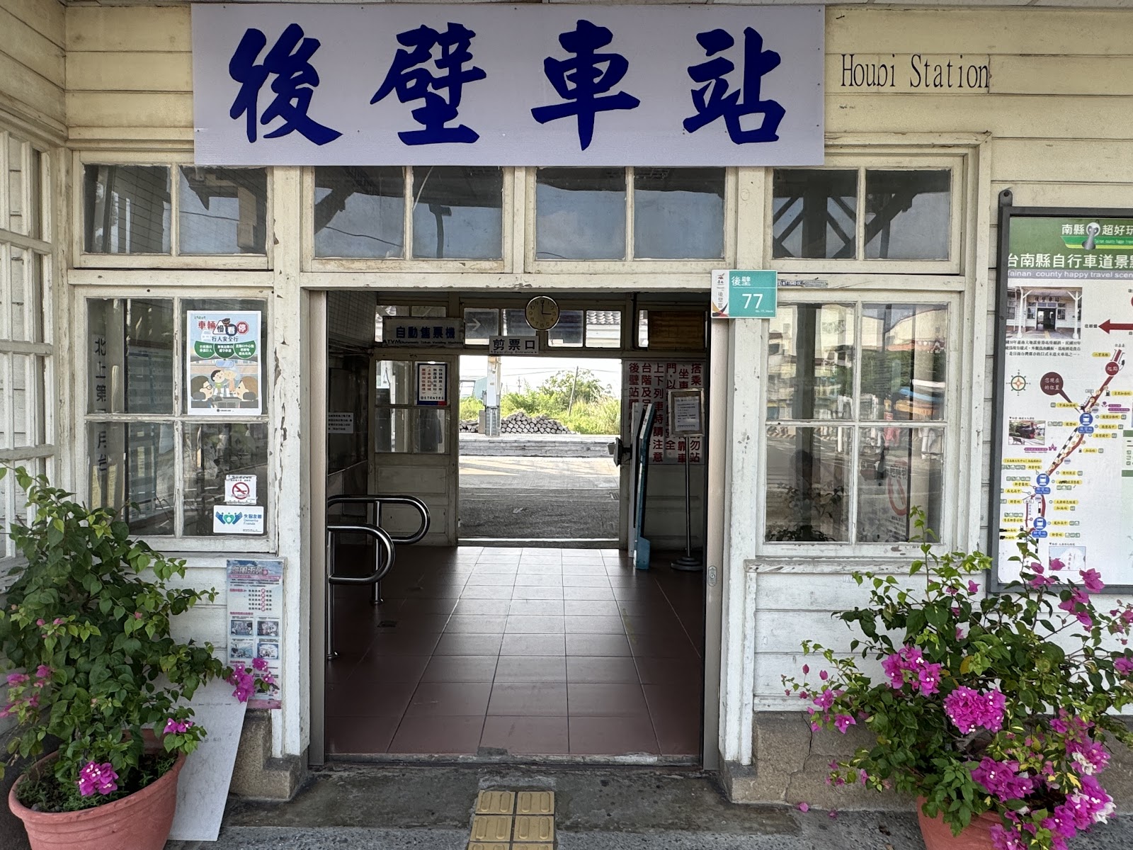 後壁車站正面入口，後壁車站藍色大字招牌，兩旁九重葛盆栽盛開