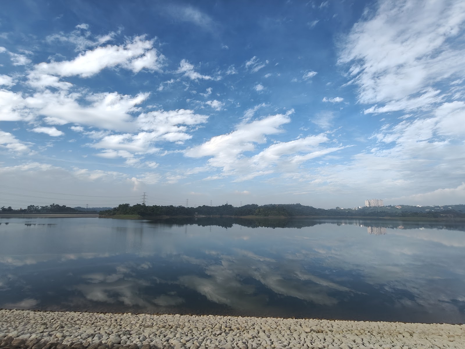 仁義潭水庫護岸卵石前景，湖面倒映藍天白雲