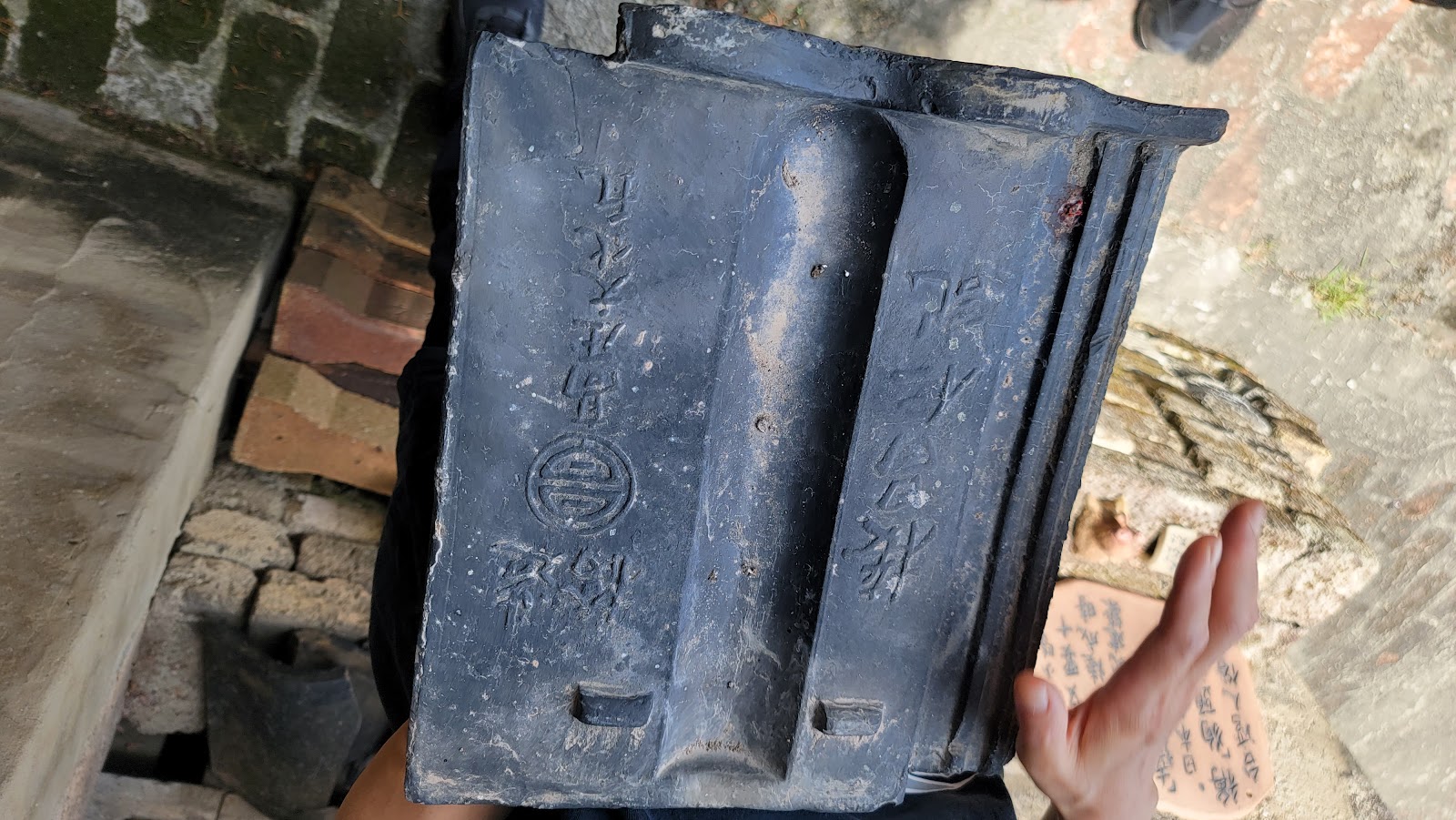 遊客手持清代陶磚瓦，刻有文字印記，背景是老窯磚牆