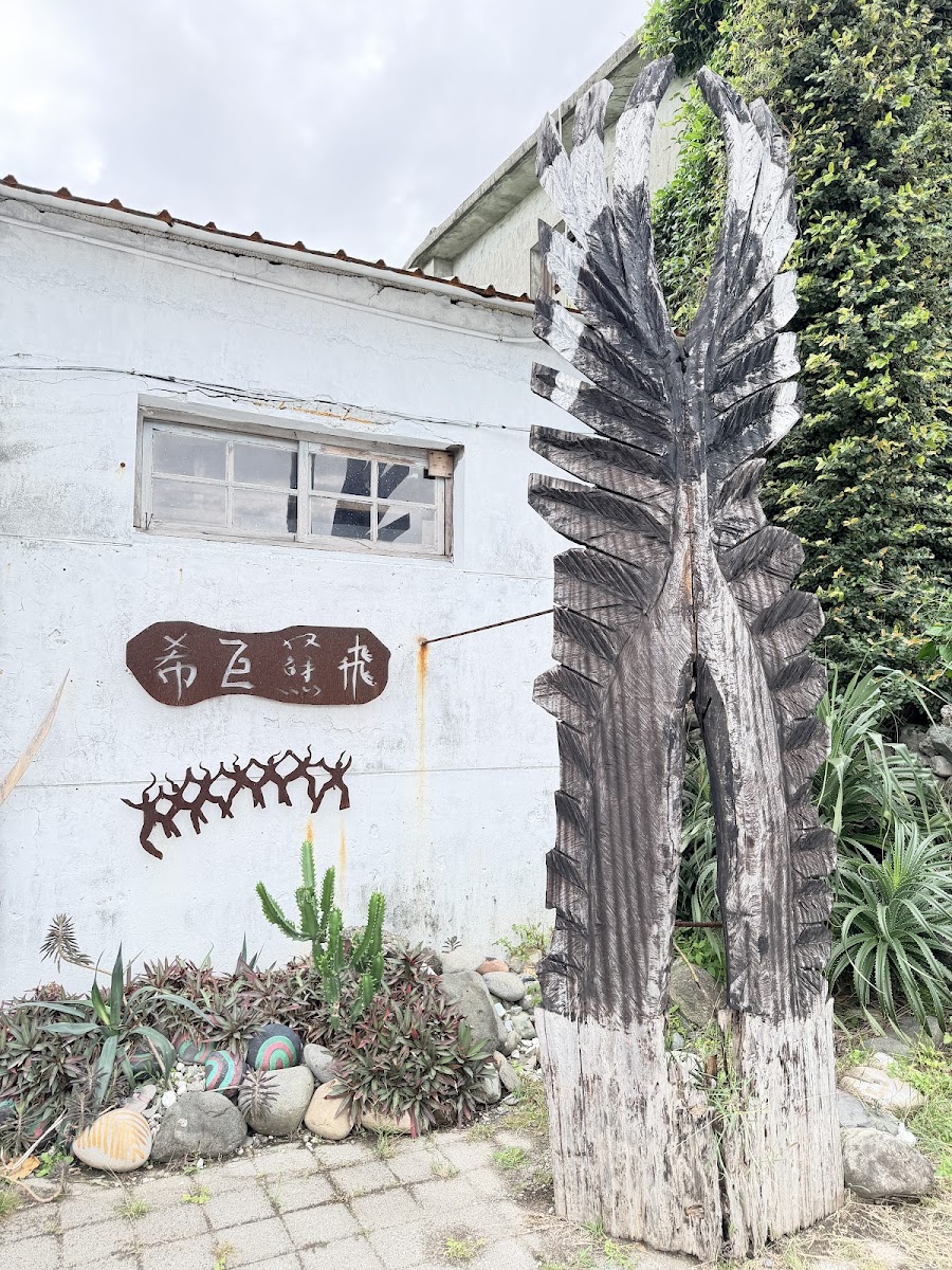 都蘭糖廠白色牆面前矗立的阿美族木雕圖騰,旁邊有裝飾植栽與彩色石頭