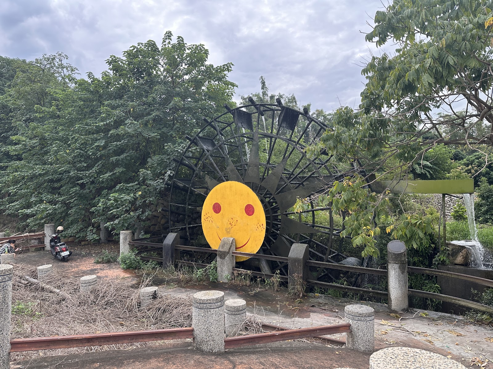 草屯水車公園黃色笑臉水車廣角,旁邊有小瀑布流水與石柱圍欄