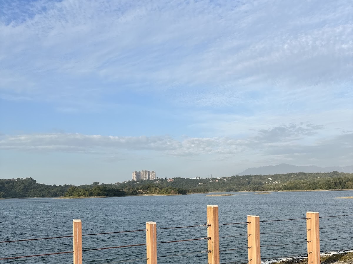 仁義潭水庫湖面全景，前景木樁圍欄，背景山坡與藍天