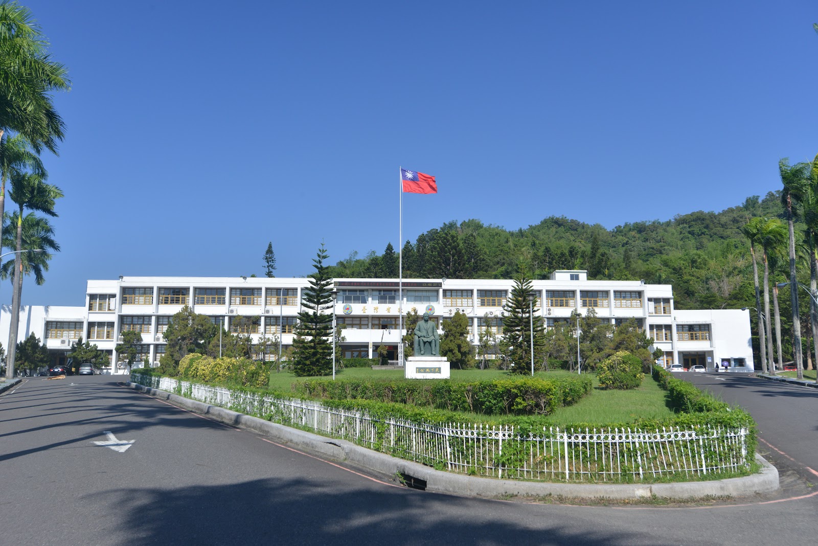 臺灣省政大樓正面廣角,白色大樓前有圓環草坪和國旗旗杆,棕欄樹圍繞,後方青翠山巒
