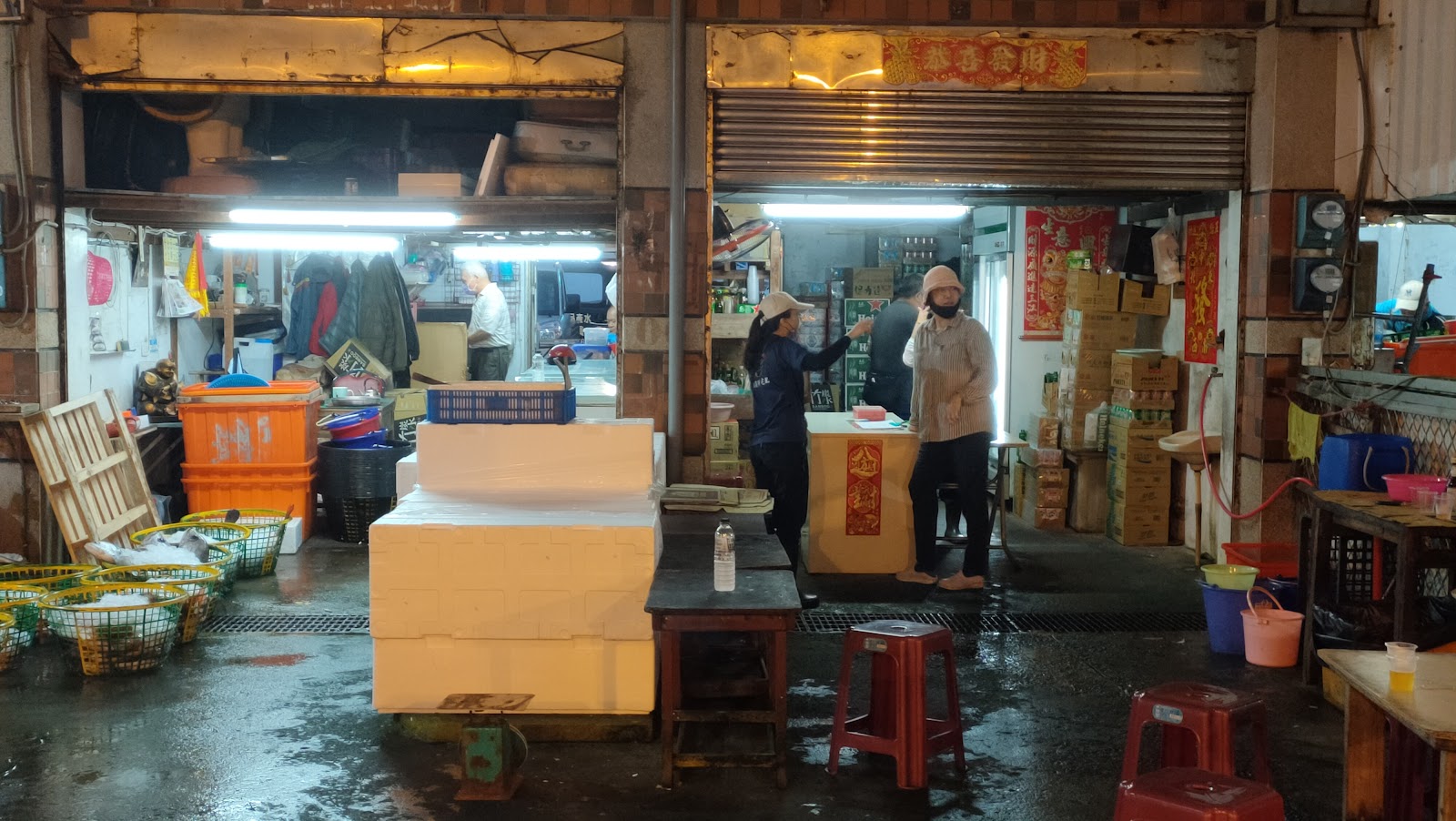 澎湖魚市場內部，昏黃燈光，販售攤位，工人搬運保麗龍魚箱，地板溼潤，充滿在地漁港氣息