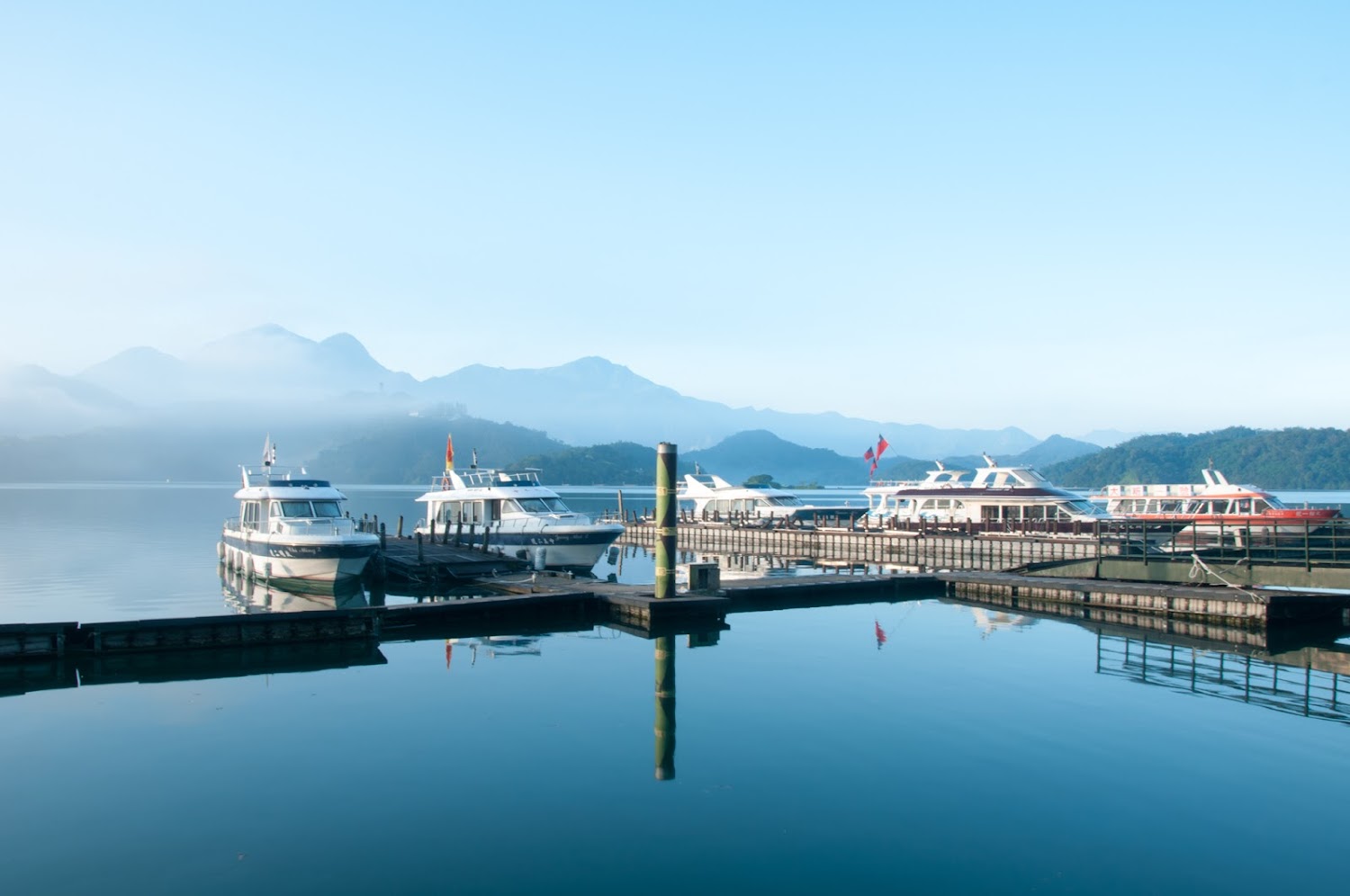 一座湖邊碼頭停著多艘遊艇與遠方山景