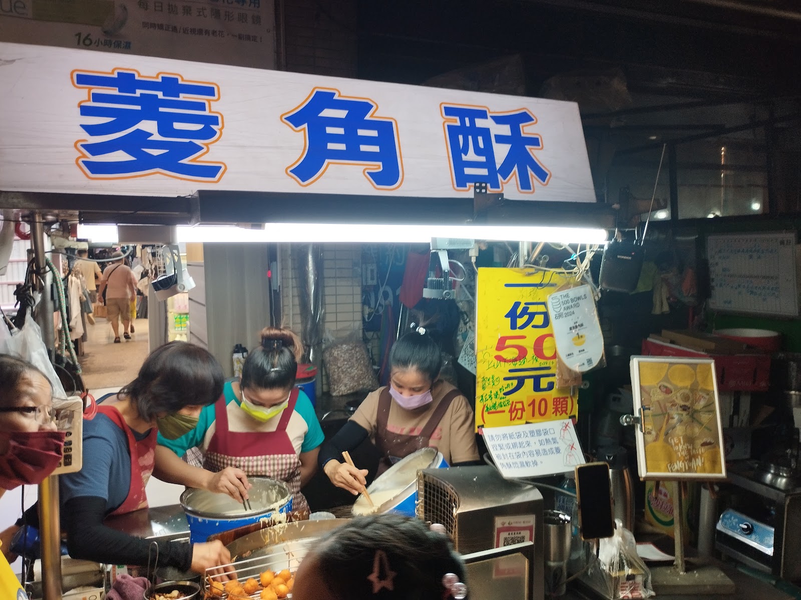 廟東川代菱角酥攤全景,三位員工忙碌操作,一份50元10顆招牌清晰可見