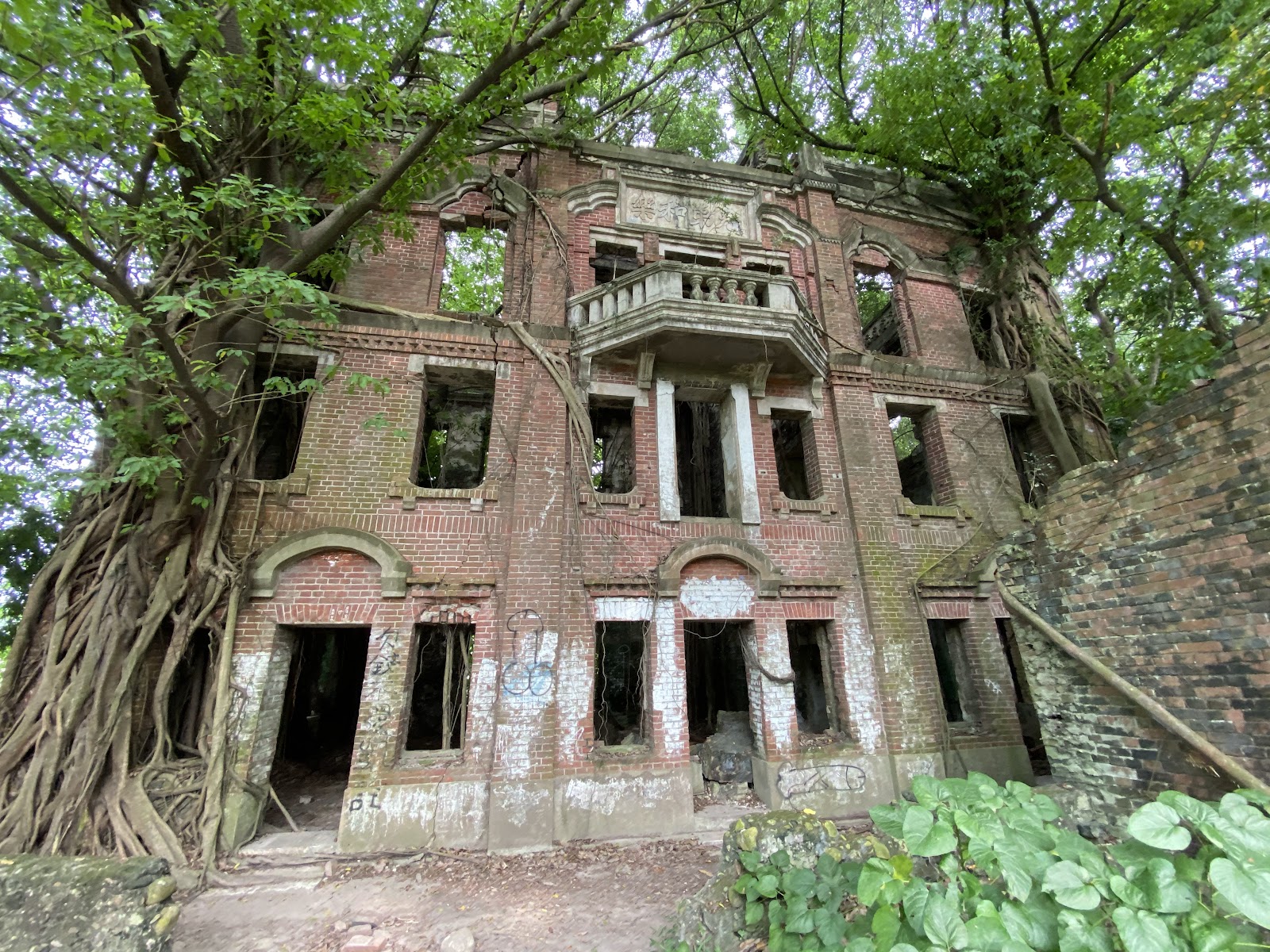 民雄鬼屋側面磚牆廢墟，樹影交疊，荒涼氛圍