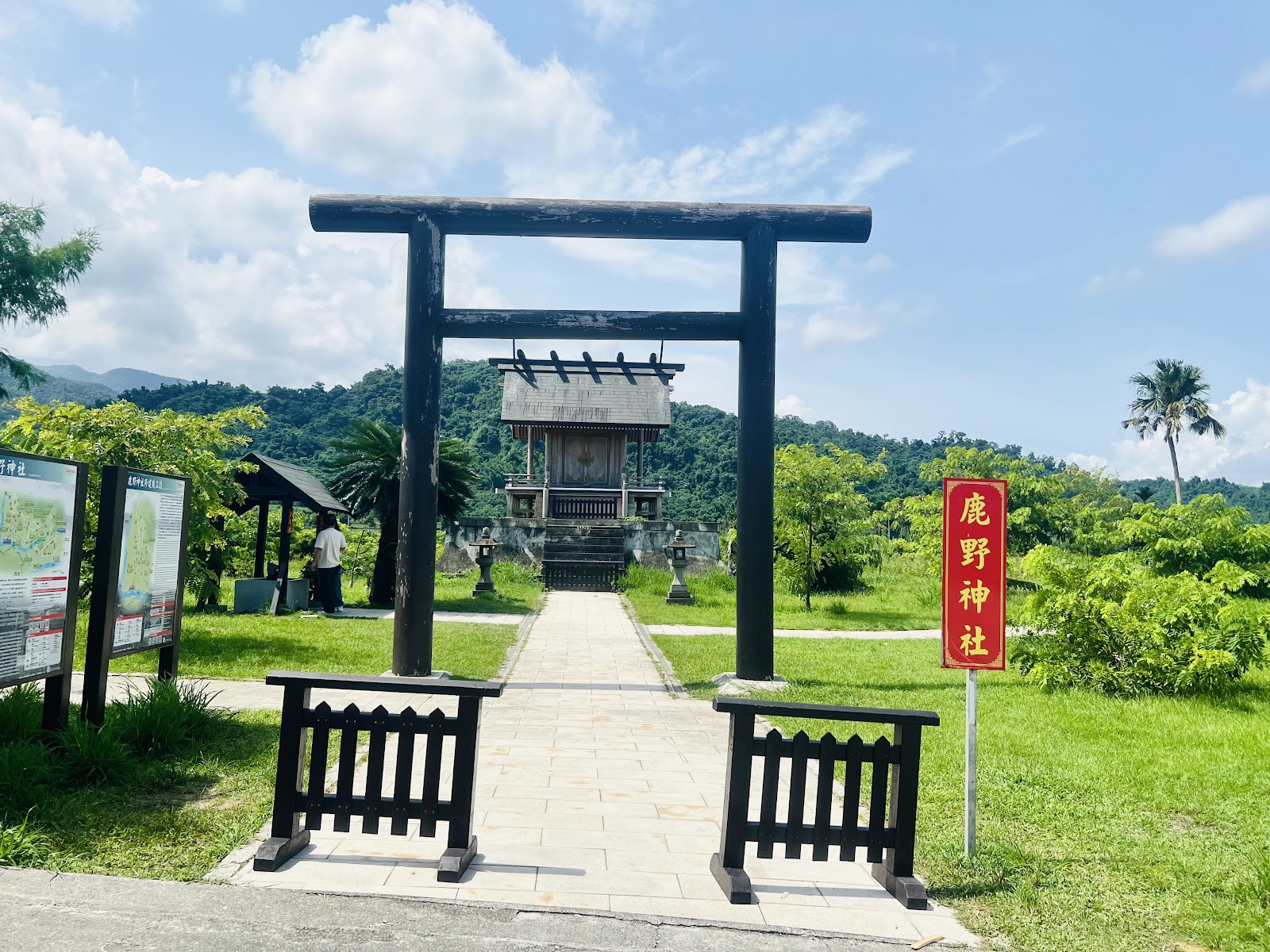 鹿野神社黑色大鳥居與石板步道,右側紅色鹿野神社標牌,藍天綠樹背景