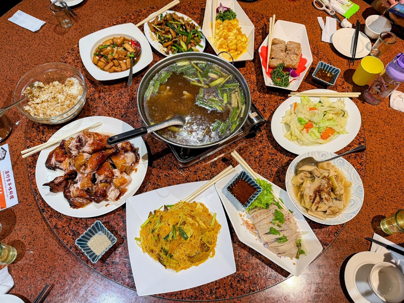 這張圖片展示一桌豐盛的中式合菜，有燒雞、炒米粉、炒青菜、火鍋、滷水白切肉、炒豆干、芋頭糕及配菜，適合多人聚餐享用。無明顯浮水印。