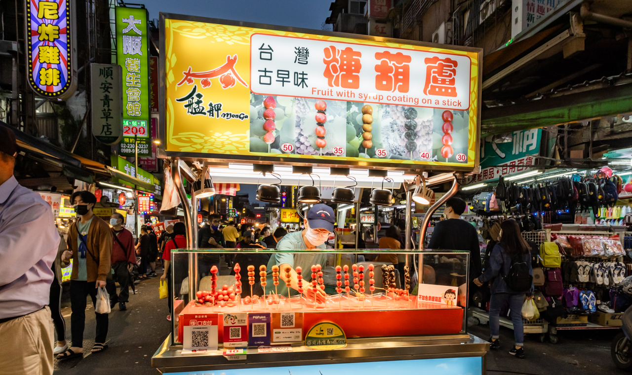 艋舺夜市古早味糖葫蘆攤位，櫥窗擺滿各式水果糖葫蘆