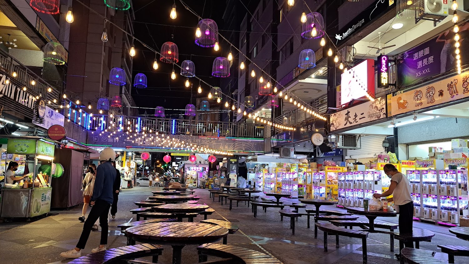 一中街夜市街道上有彩色燈籠、娃娃機與餐飲座位，氣氛年輕熱鬧
