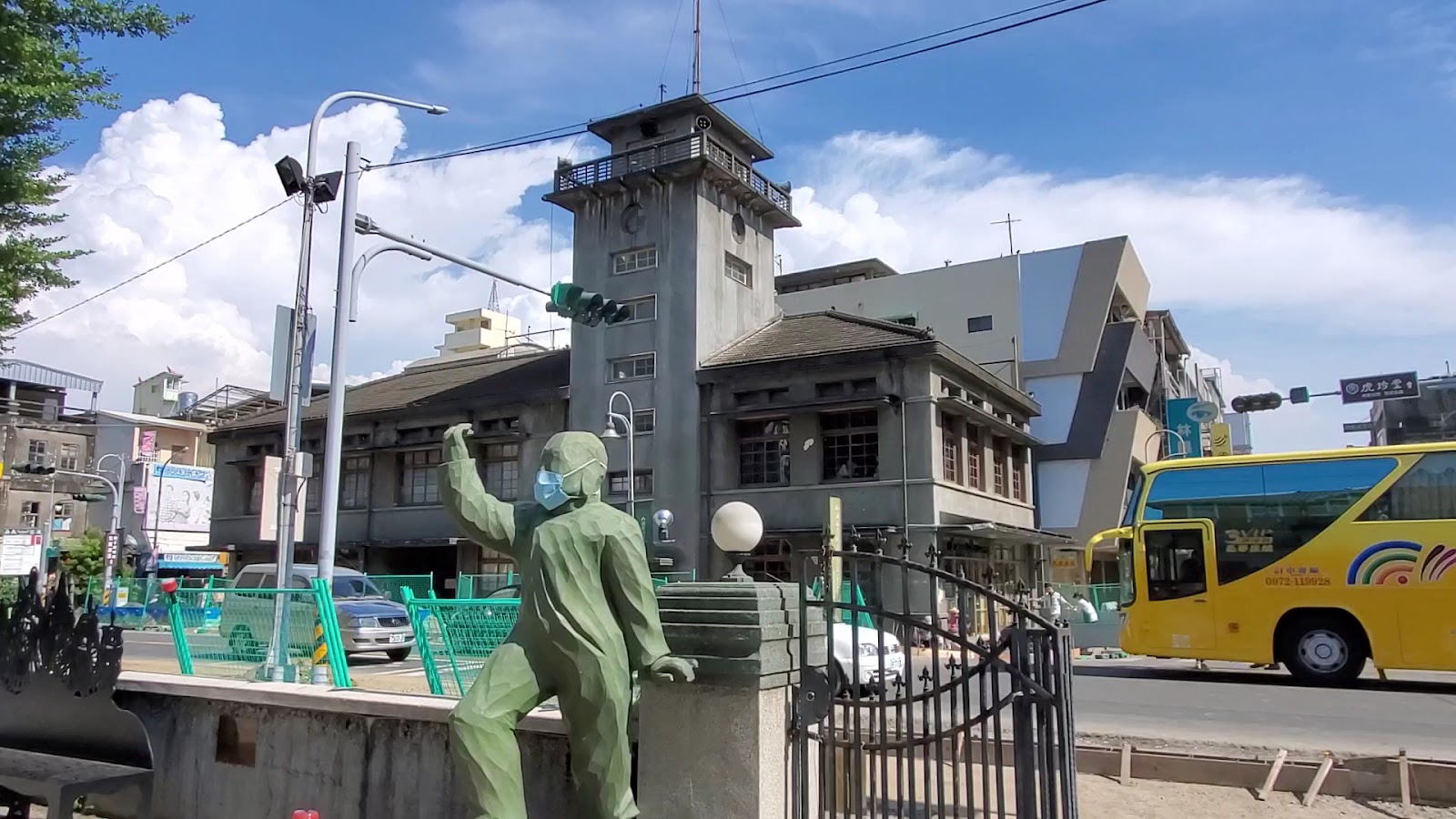 虎尾合同庭舍街景，灰色日式建築有鐘塔，前景有銅像雕塑