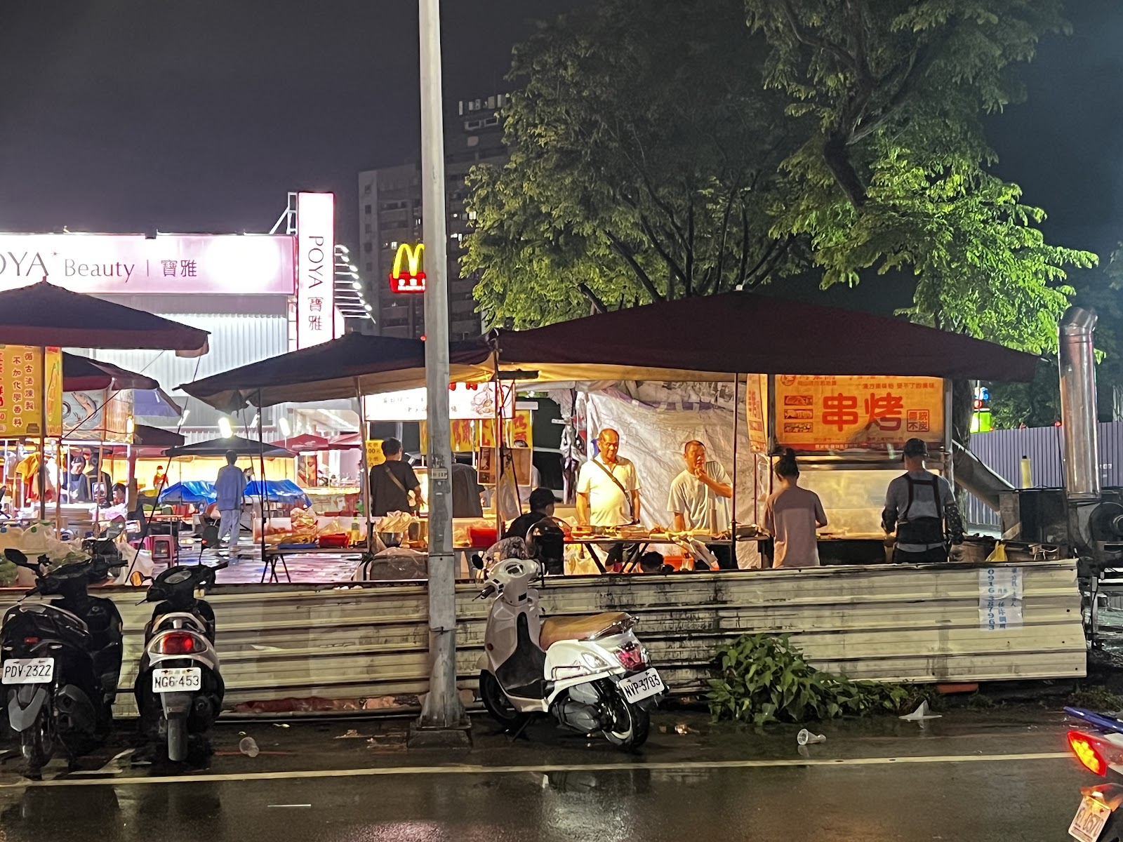 路竹夜市夜間串烤攤位,背景是POYA和麥當勞招牌,前景停放機車