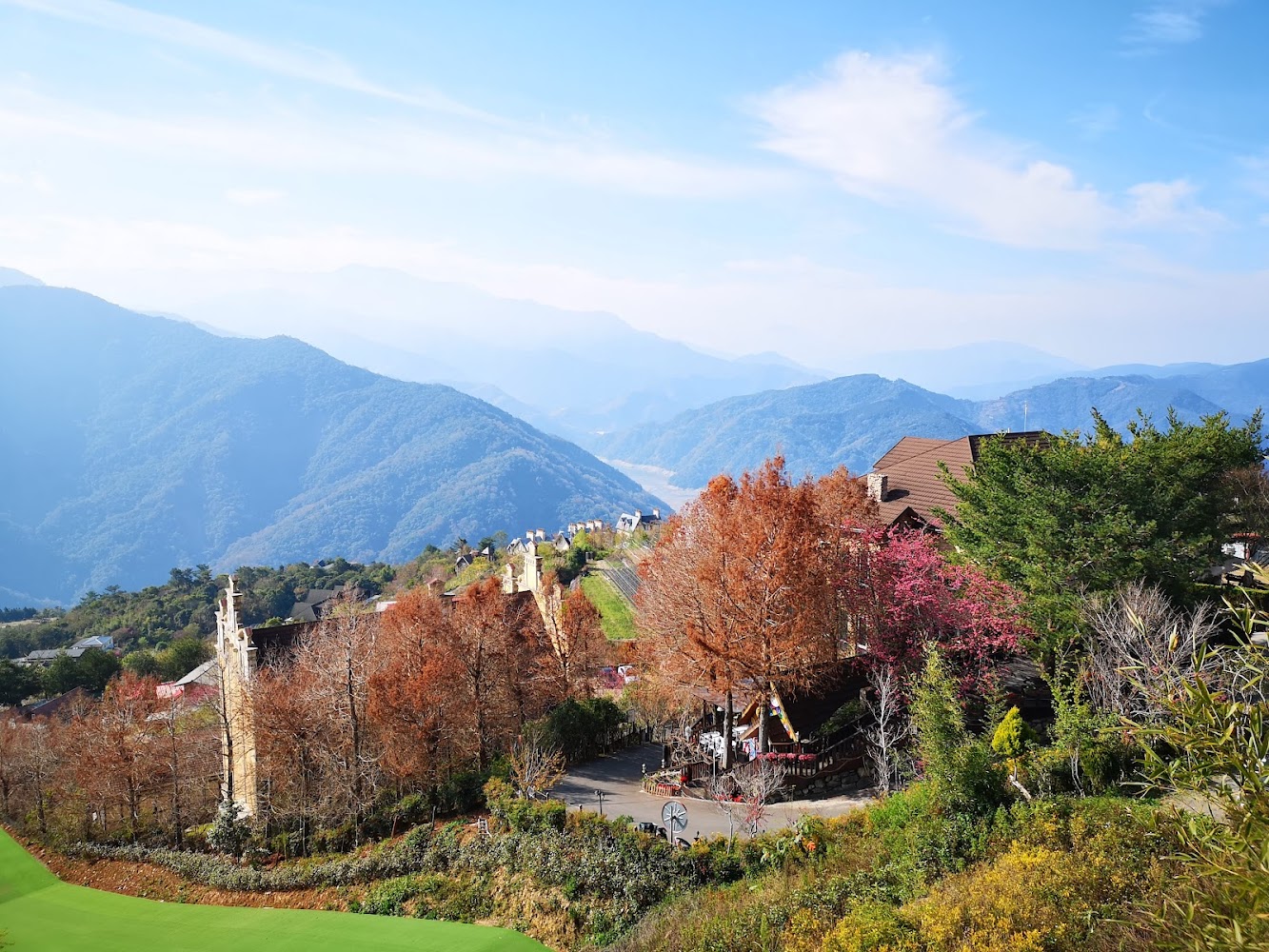 前景有秋冬色彩樹林與綠地，點綴建築物的山景