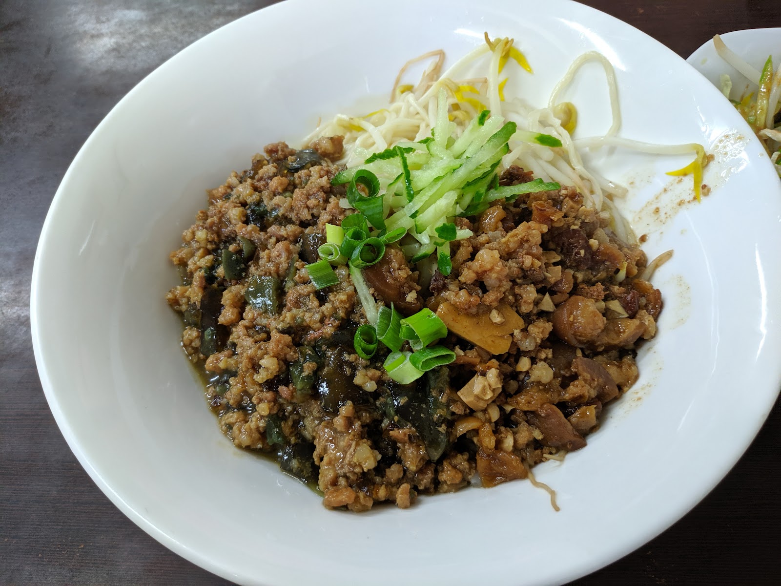 旭家私廚招牌肉燥醬拌麵，白色碗盛裝配黃瓜絲、豆芽菜與蔥花