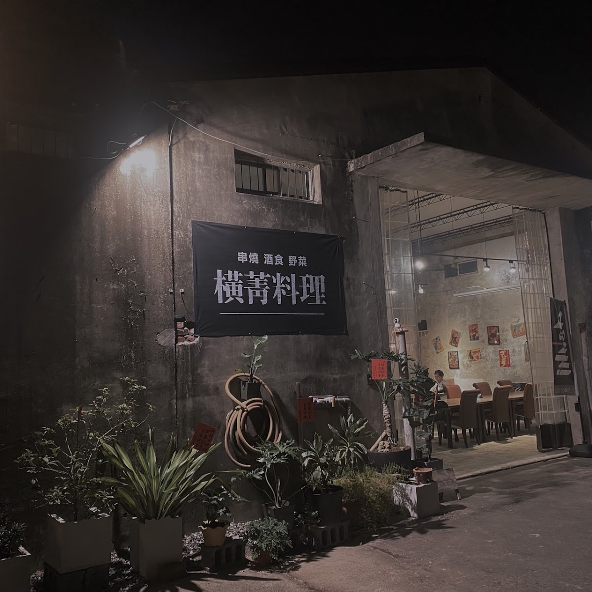 橫菁料理夜晚外觀，水泥牆上掛著招牌，植栽點綴工業風入口