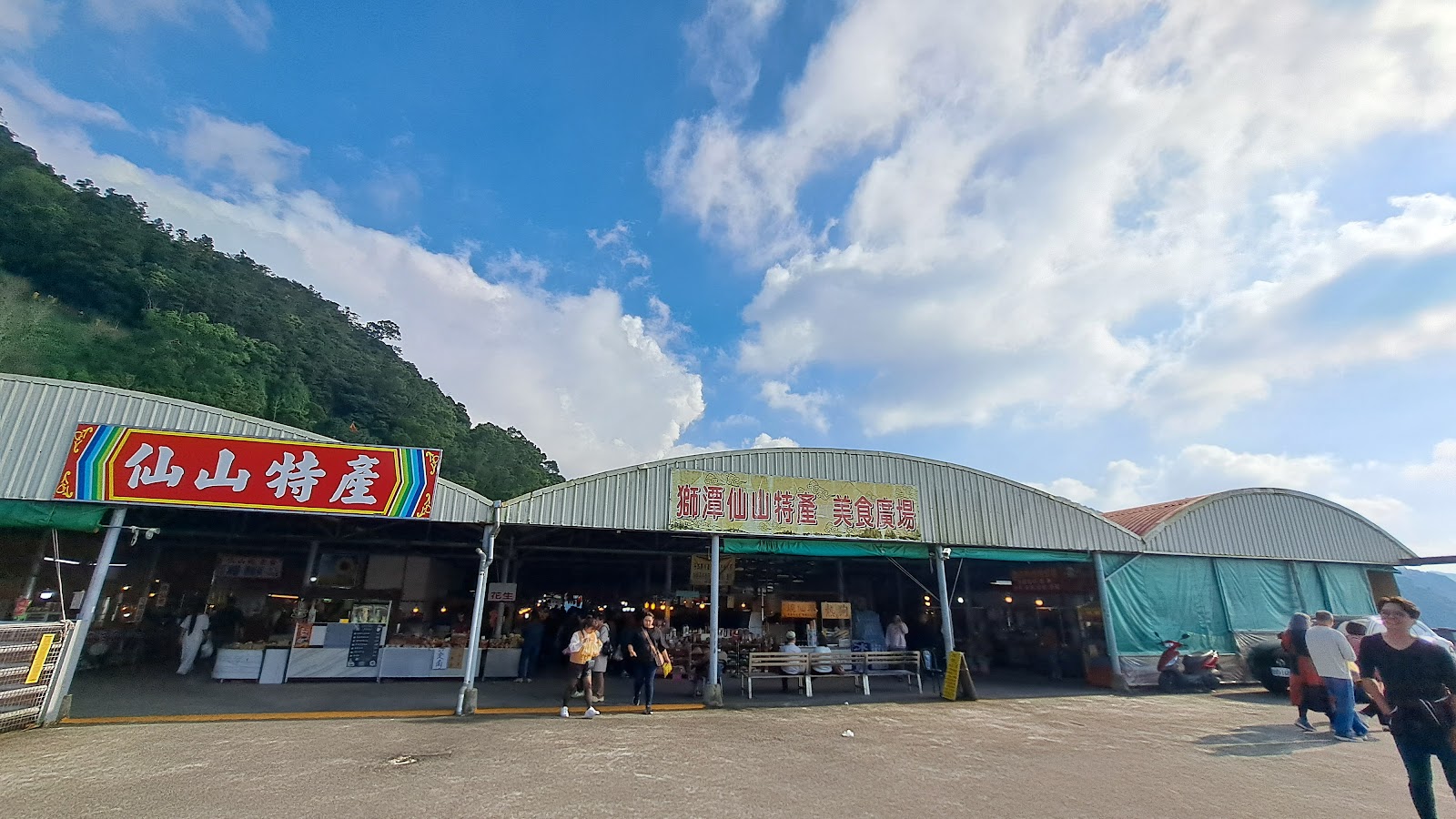 仙山美食特產廣場外觀，仙山特產招牌，攤位遊客人潮，山景藍天