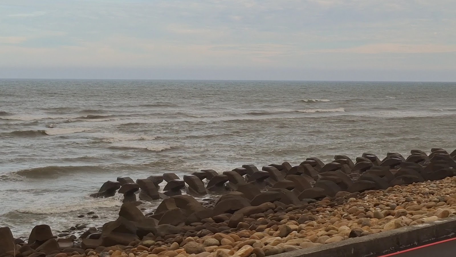 新屋海岸消波塊與礫石灘，海浪拍打岸邊，海天一色