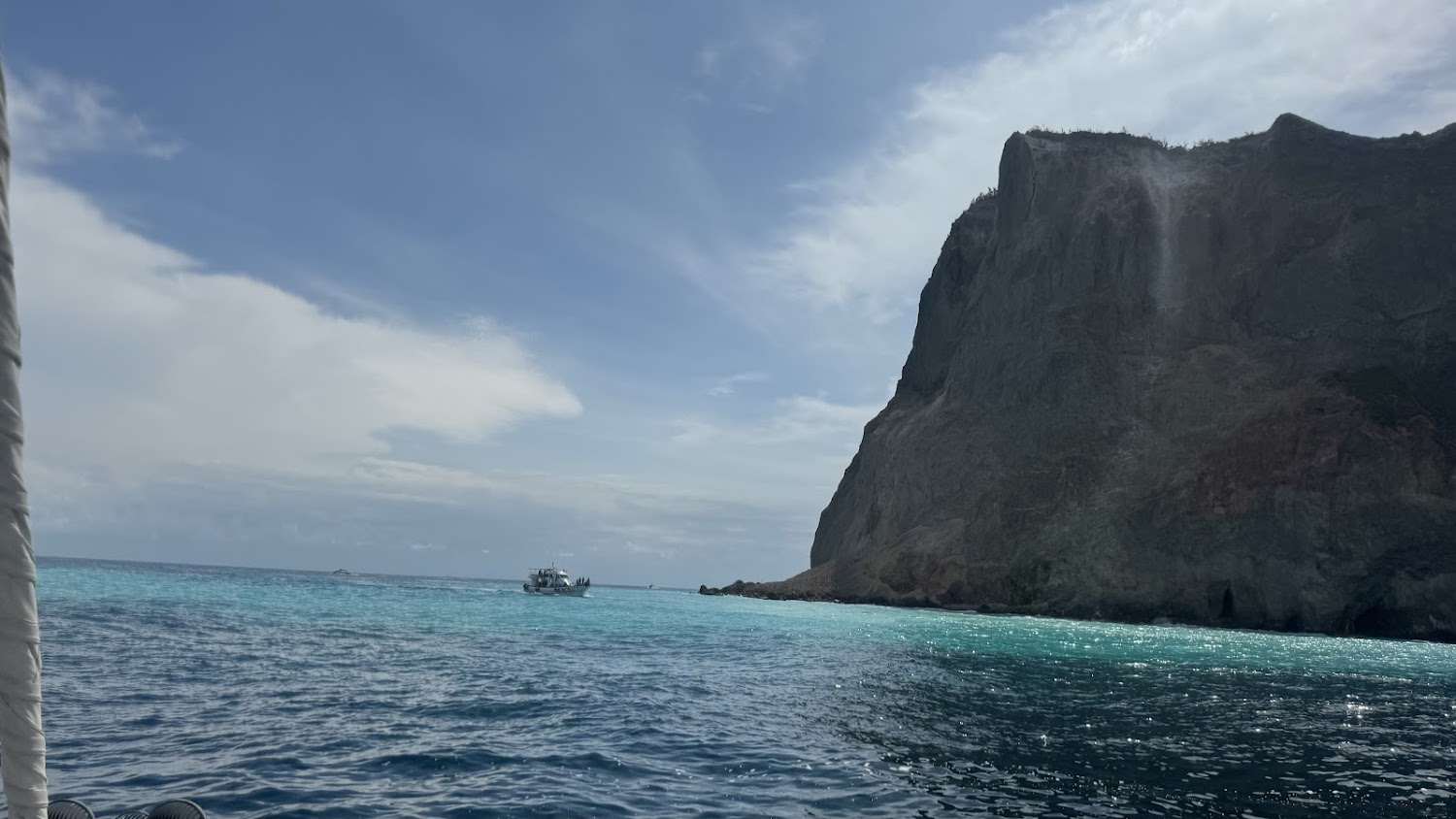 小船航行在藍綠色海面旁邊是高聳岩壁