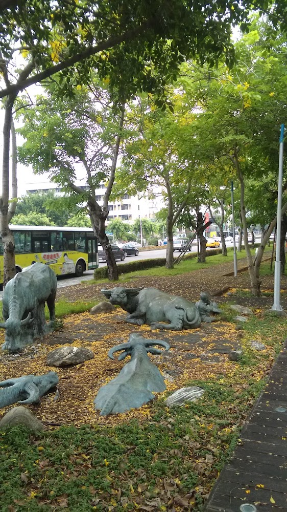 樹蔭步道旁的水牛銅像與都市街景背景