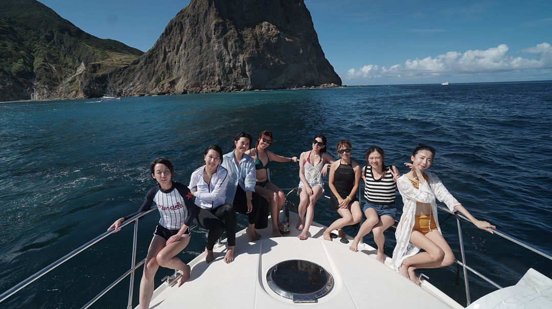 八位女性坐在船頭與龜山島岩壁合影