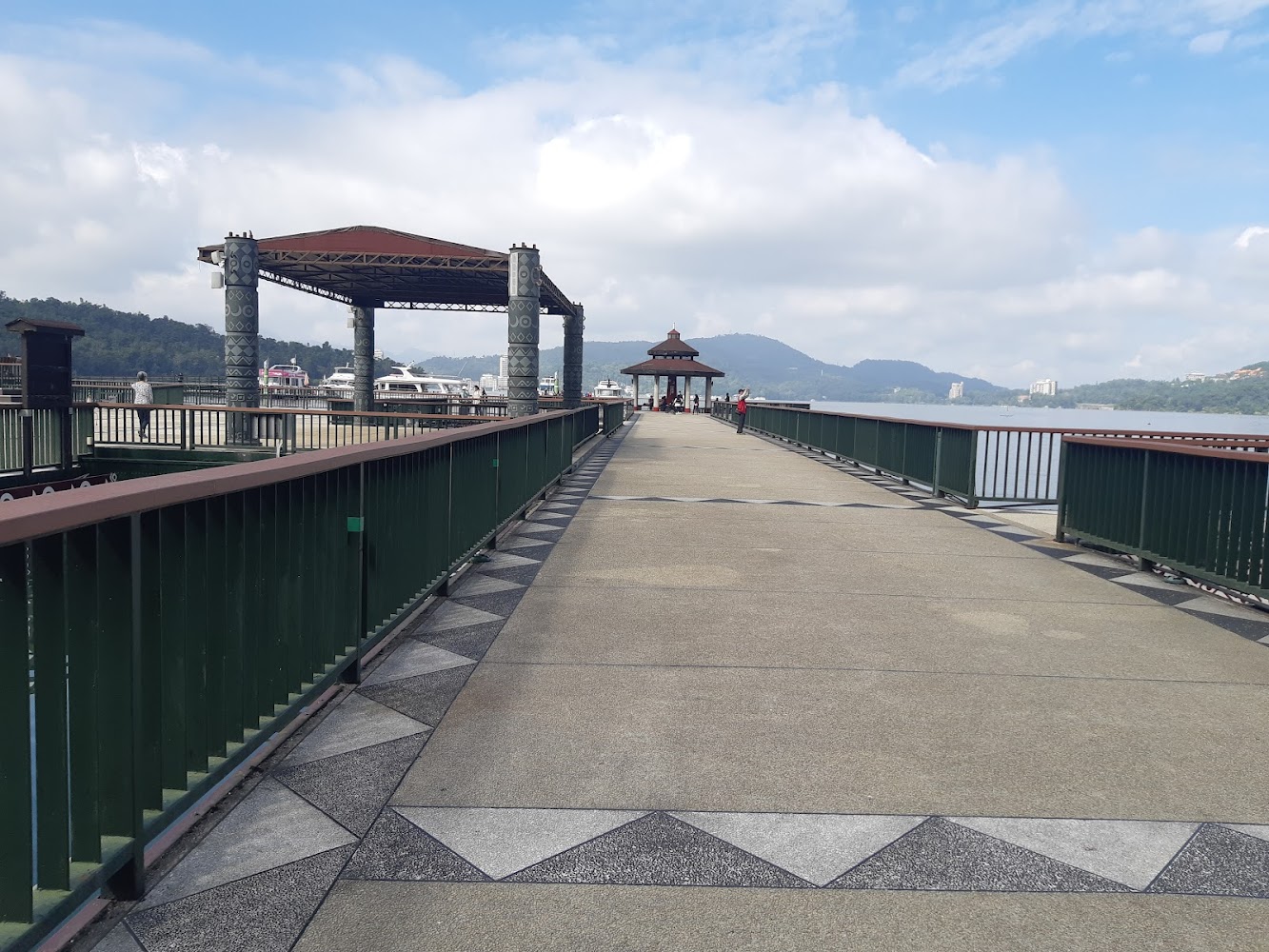 寬闊湖邊步道有涼亭柱子裝飾背後湖泊山脈遊艇
