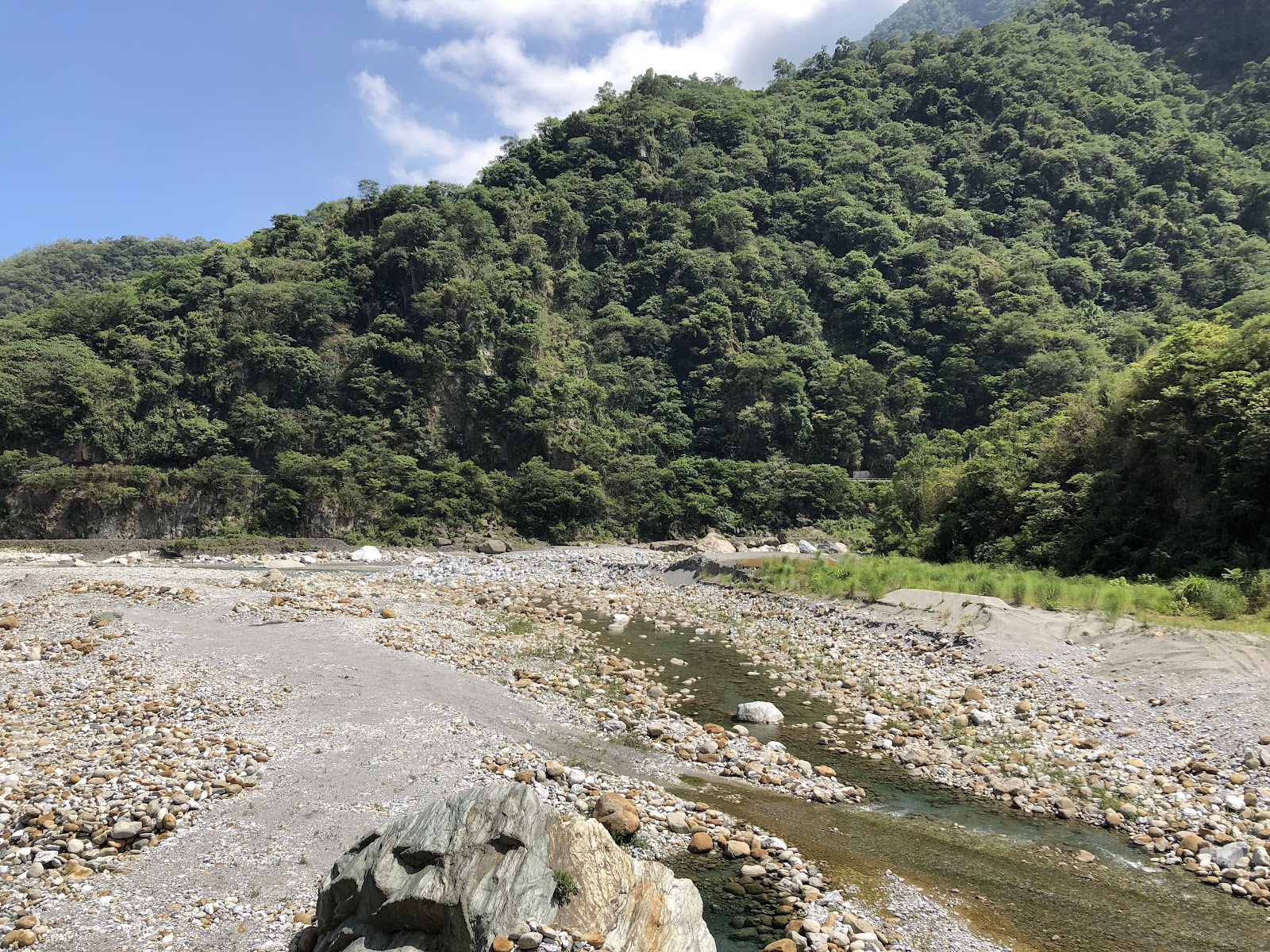 慕谷慕魚河床礫石廣闊，遠方翠綠山坡藍天白雲