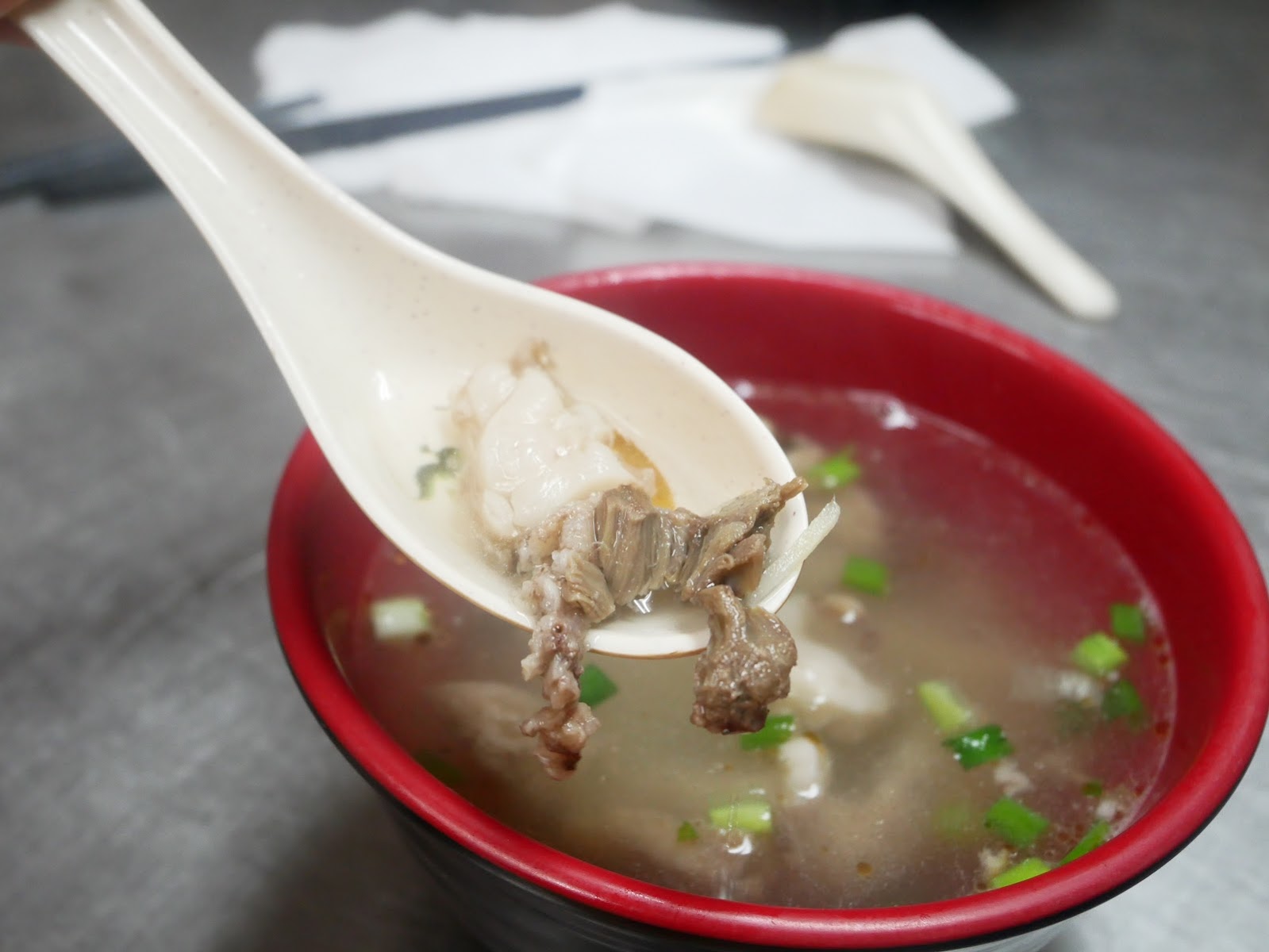 洪記中港肉圓骨仔肉湯，白瓷湯匙舀起骨仔肉，紅色碗，清澈湯頭撒蔥花