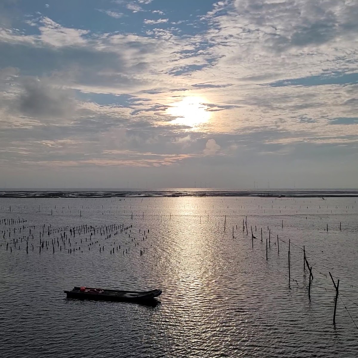 芳苑日落眺望臺夕陽美景，陽光穿雲灑落海面，竹樁與小木舟剪影