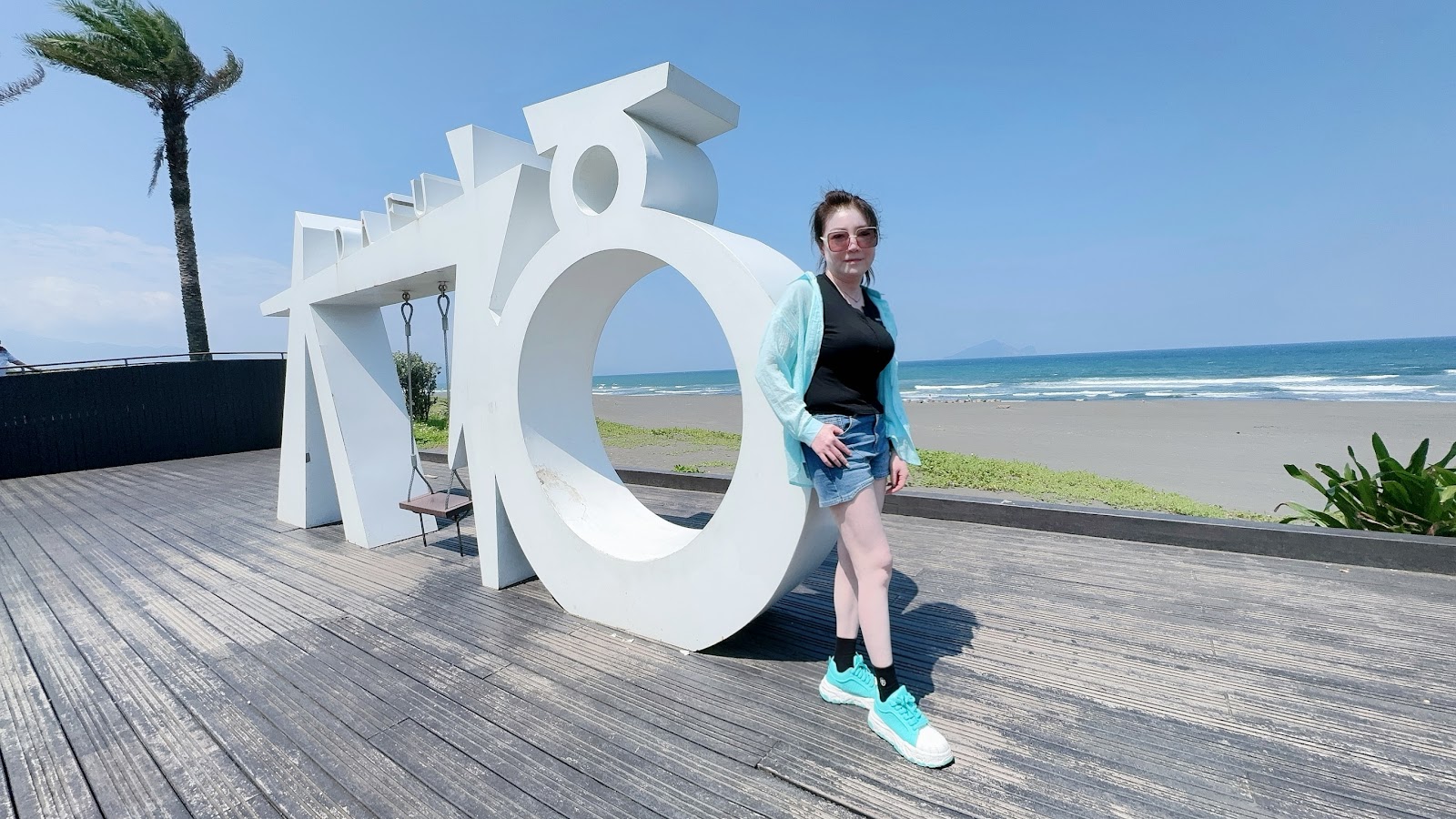 女生站在大福碉堡觀景台白色大型裝置藝術前拍照,背景是太平洋