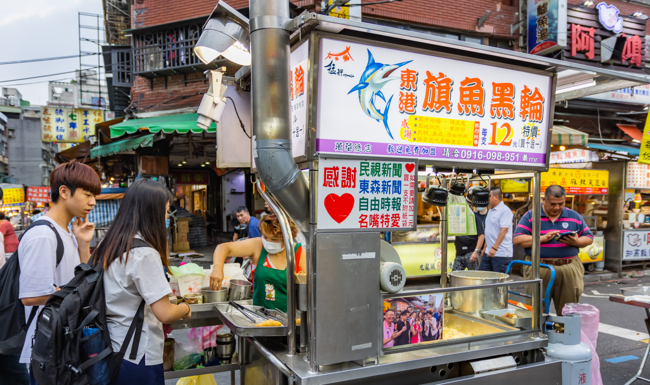 艋舺夜市東港旗魚串攤位，招牌醒目，客人排隊