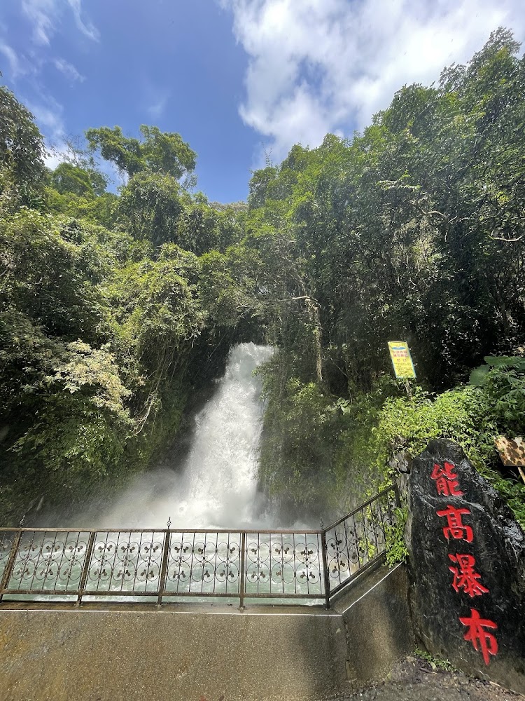 這張圖片主要是一個位於森林中的瀑布,名字為能高瀑布(從石頭上的紅字可見),水流湍急,旁邊有欄杆保護,周圍環繞著茂密的樹林,天氣晴朗。圖片沒有浮水印。