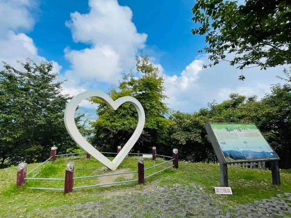 大型白色愛心裝置藝術，背景是綠色樹林和藍天白雲