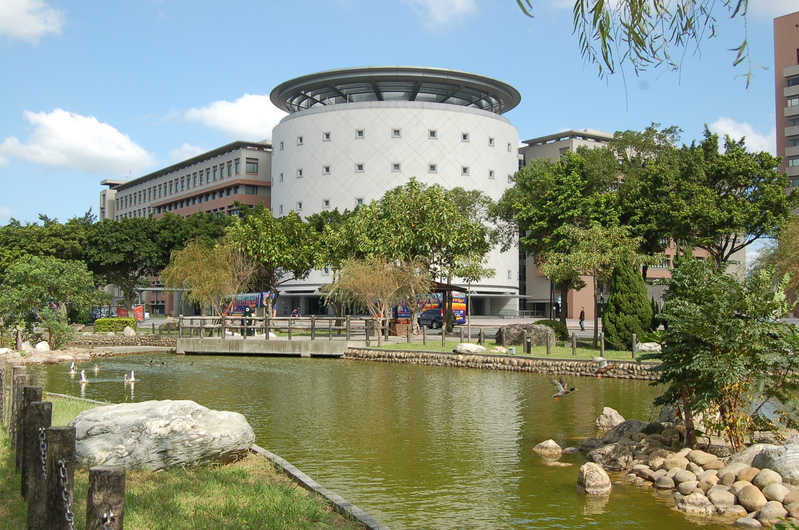 這張圖片主要有一座現代化圓形建築,前方有池塘、石頭和綠樹,環境寧靜。池塘中可見幾隻鳥,整體氛圍自然且舒適。圖片沒有浮水印。