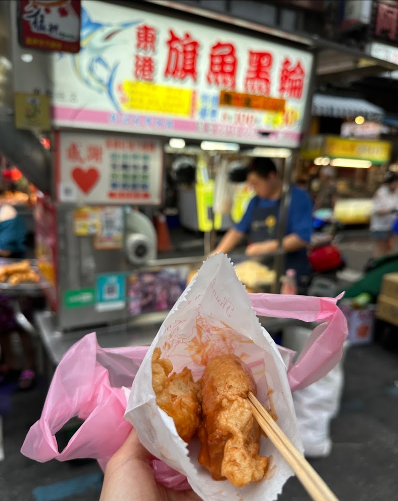 手拿炸旗魚黑輪，背景可見夜市招牌