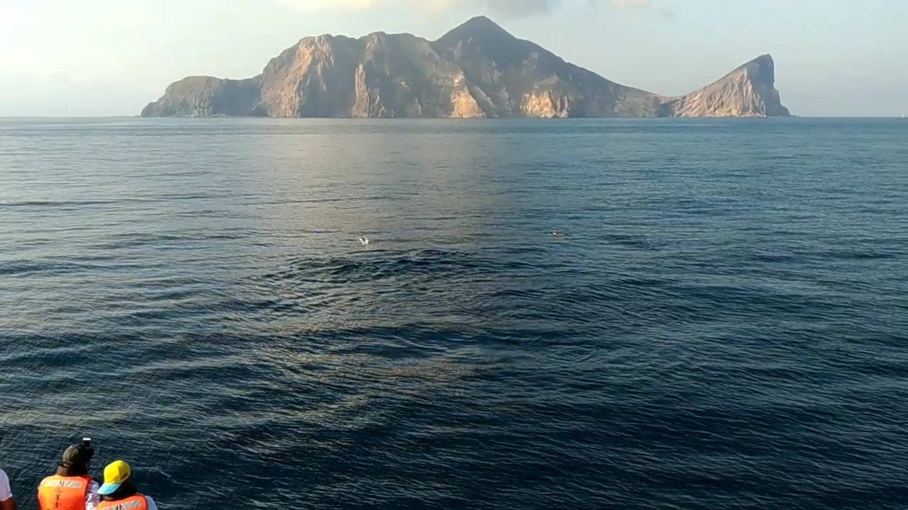 兩位穿救生衣的遊客站在船邊遠望龜山島