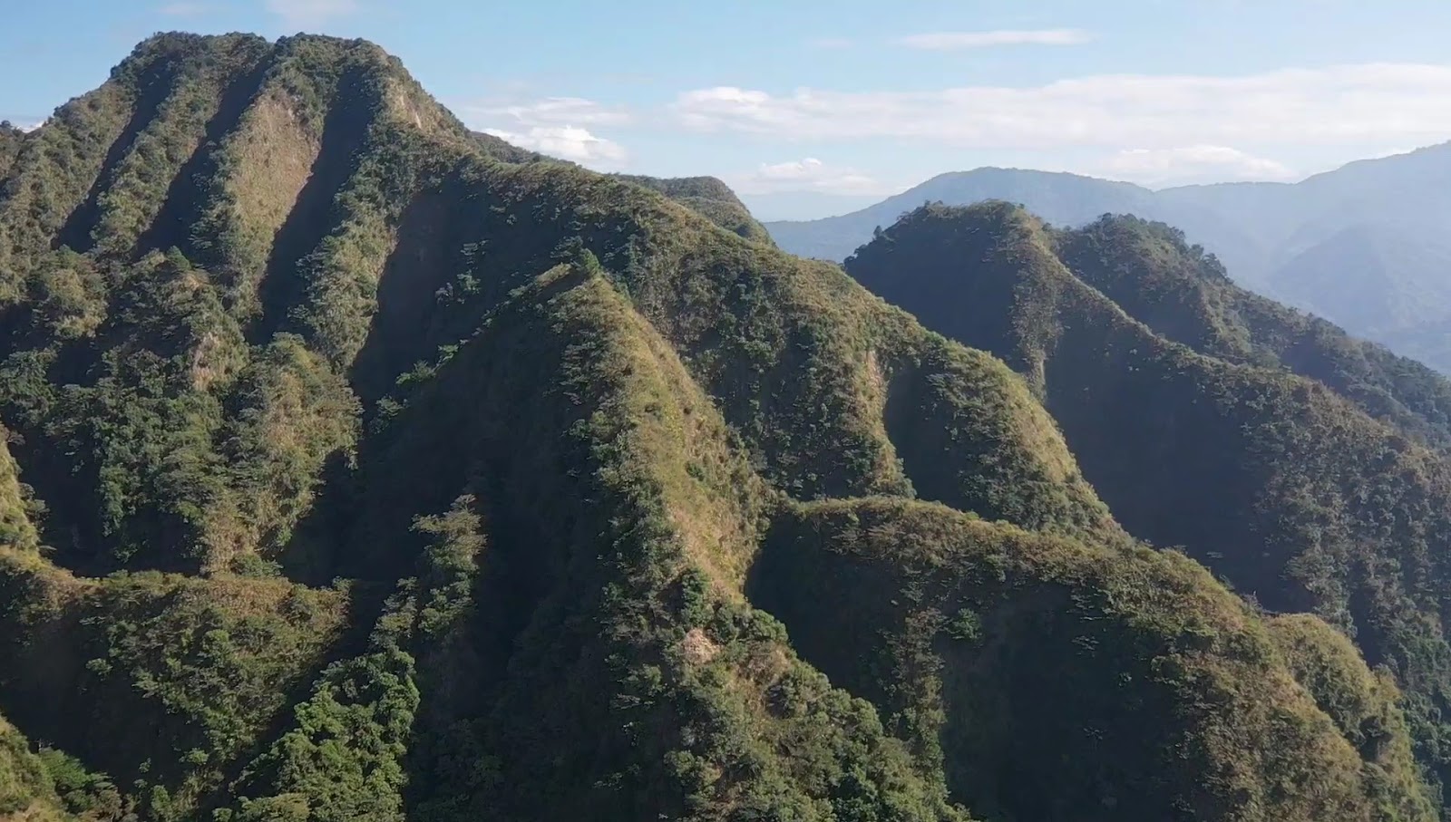 九九峰山脈空拍全景,連綿青翠山峰層疊,藍天白雲