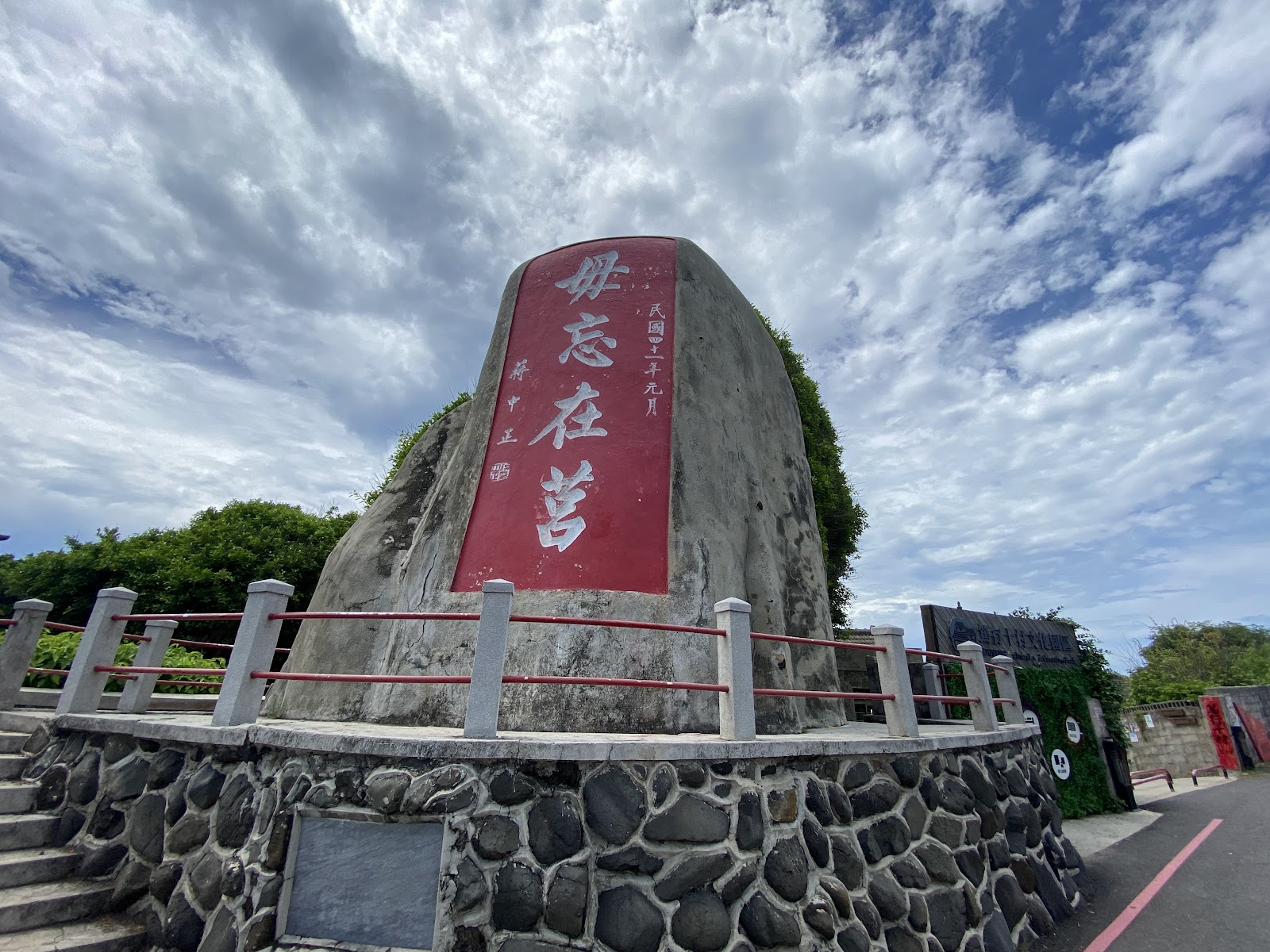 澎湖篤行十村入口玄武岩石碑，刻有毋忘在莒紅字，藍天白雲綠樹環繞