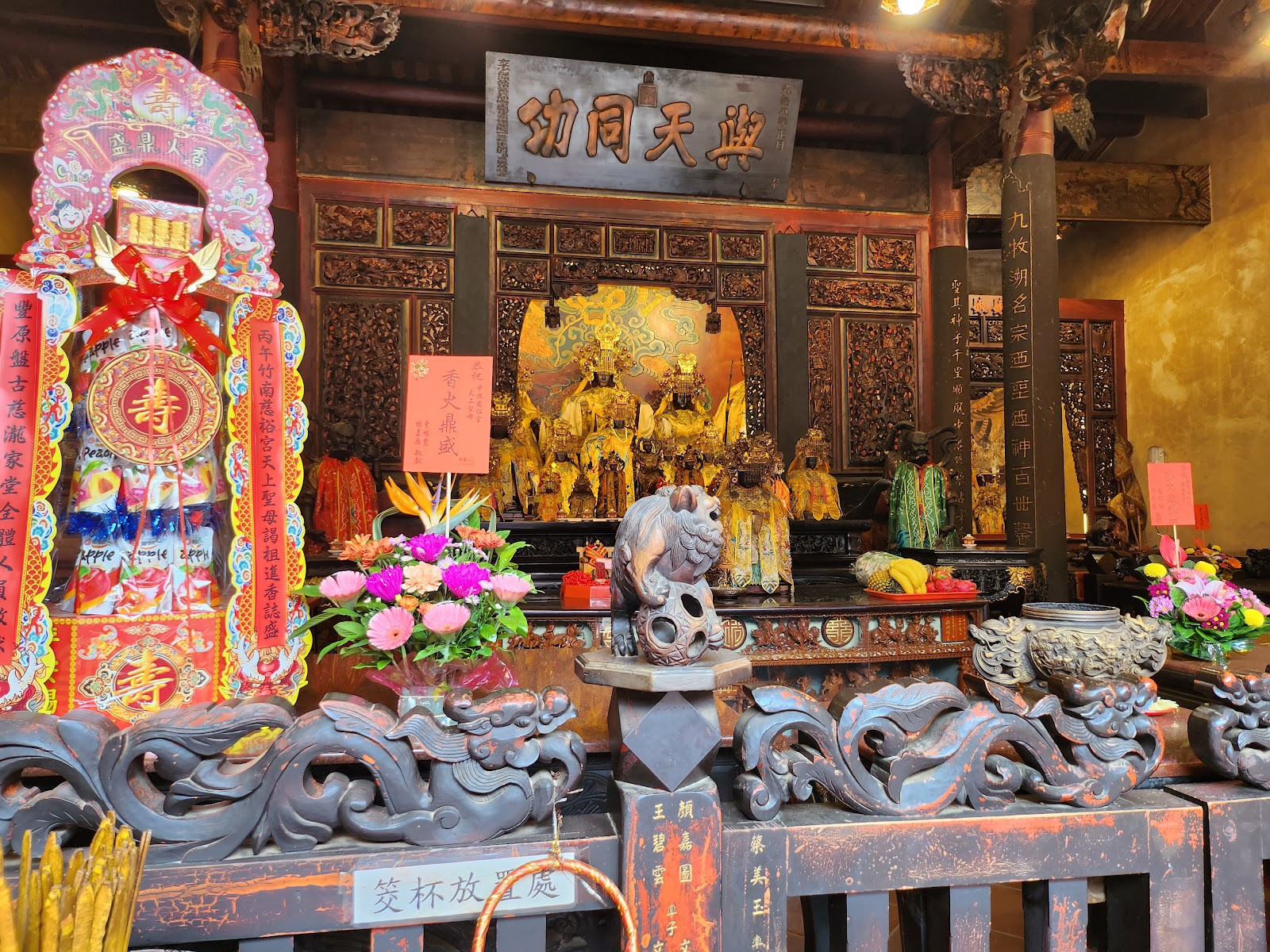 竹南中港慈裕宮大殿正廳，神像前有供桌、鮮花、壽字燈，橫匾寫著興天同功