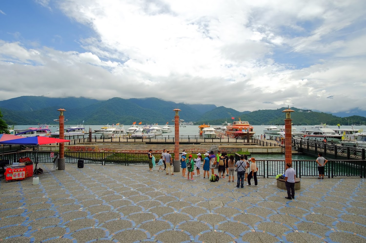 湖邊碼頭遊客與攤販前方壯麗山景