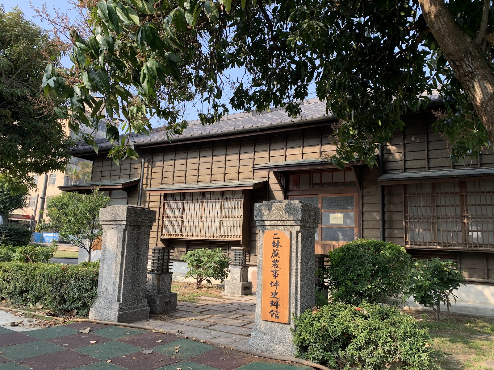 二林蔗農事件史料館入口，石造門柱上有橘色牌匾，木造日式建築，庭園植栽