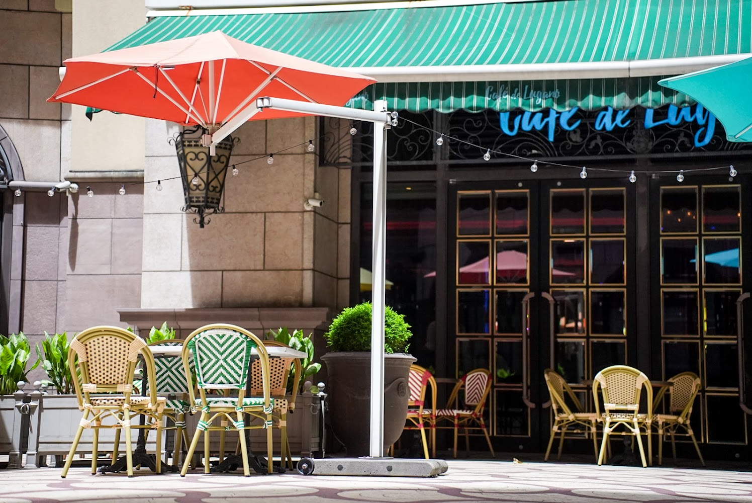 Café de LUGANO戶外座位區,有遮陽傘與編織椅,氛圍悠閒。