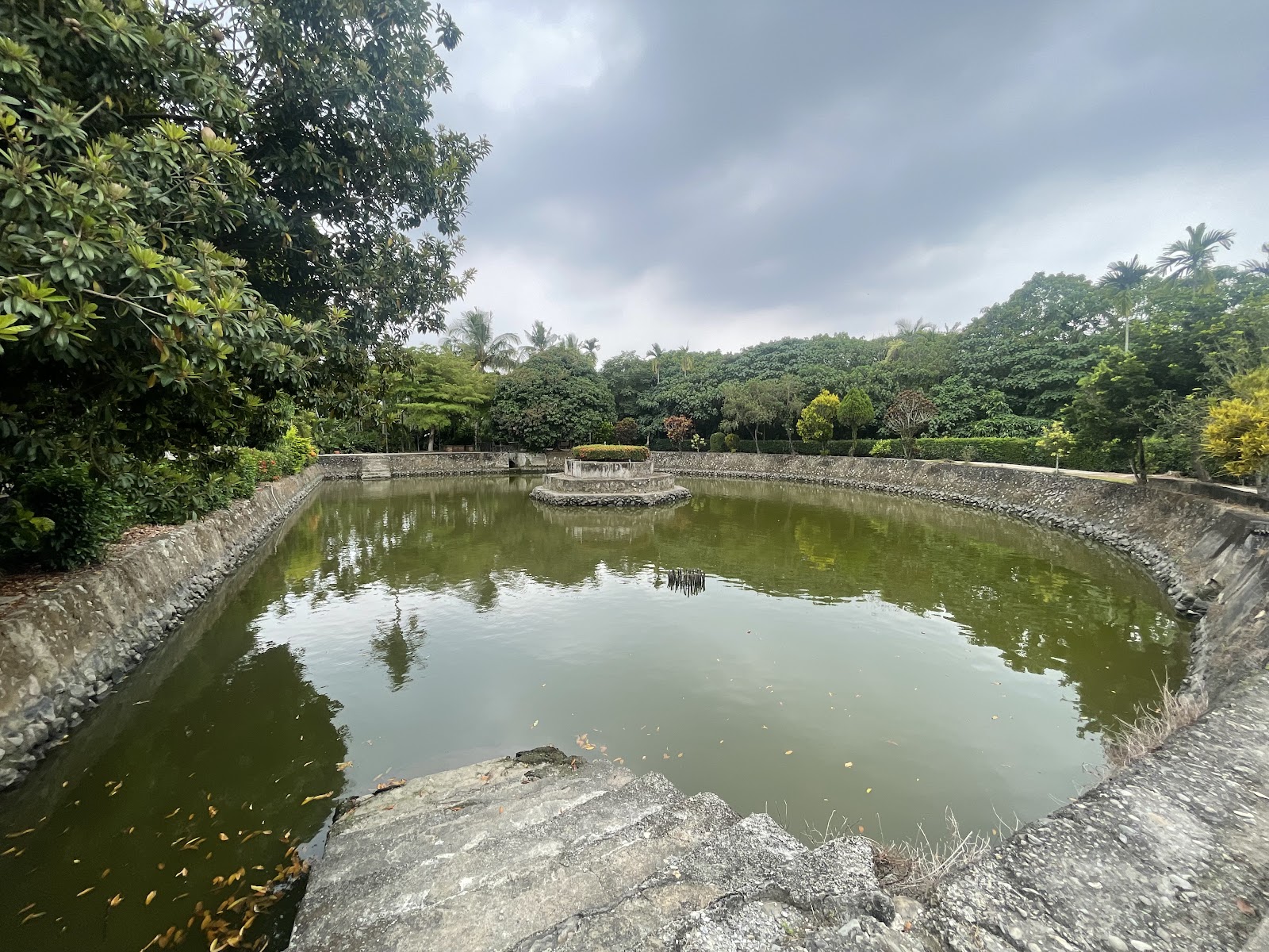 五溝水半月池，半圓石砌水池，中央小島，綠樹環繞，平靜水面映倒影