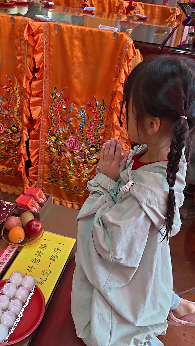 澎湖天后宮殿內，小女孩雙手合十向媽祖祈禱，供桌供品莊嚴