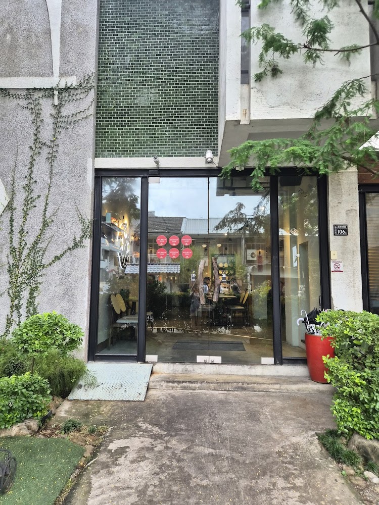 這張圖片主要顯示一間店面的正門，玻璃門上貼有紅色圓形貼紙，門外兩側有綠色植物點綴，門旁放有雨傘桶，整體環境整潔舒適。圖片未見明顯浮水印。