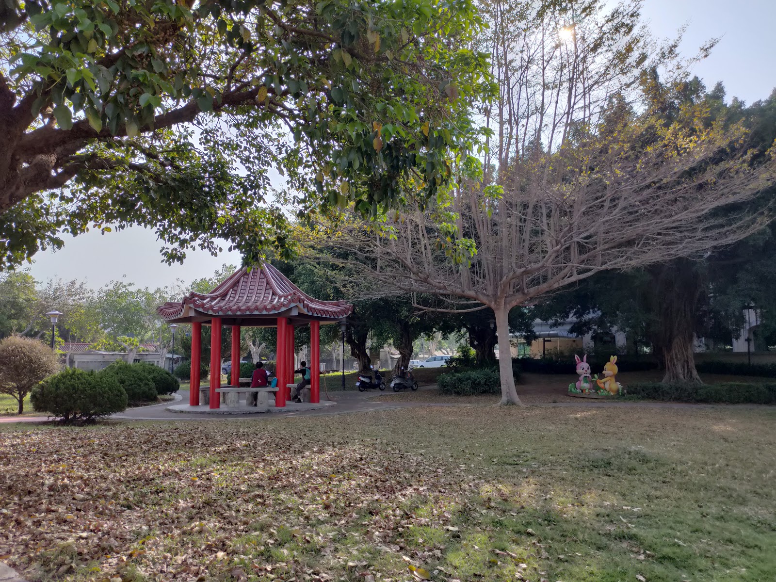 中興新村親情公園六角涼亭,朱紅色柱子金色屋頂,落葉鋪地,旁有公仔裝置