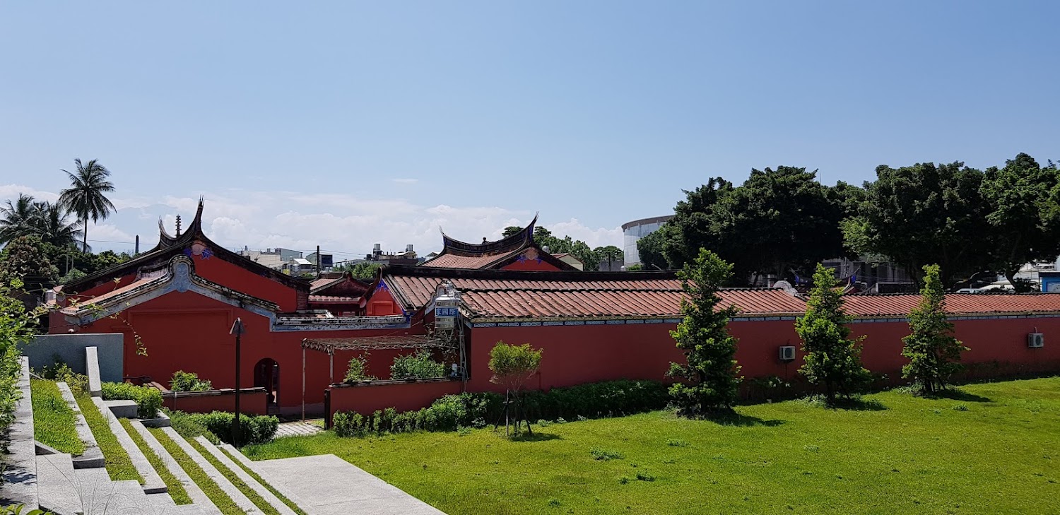 傳統紅色寺廟建築,前方草地整齊,天空晴朗。