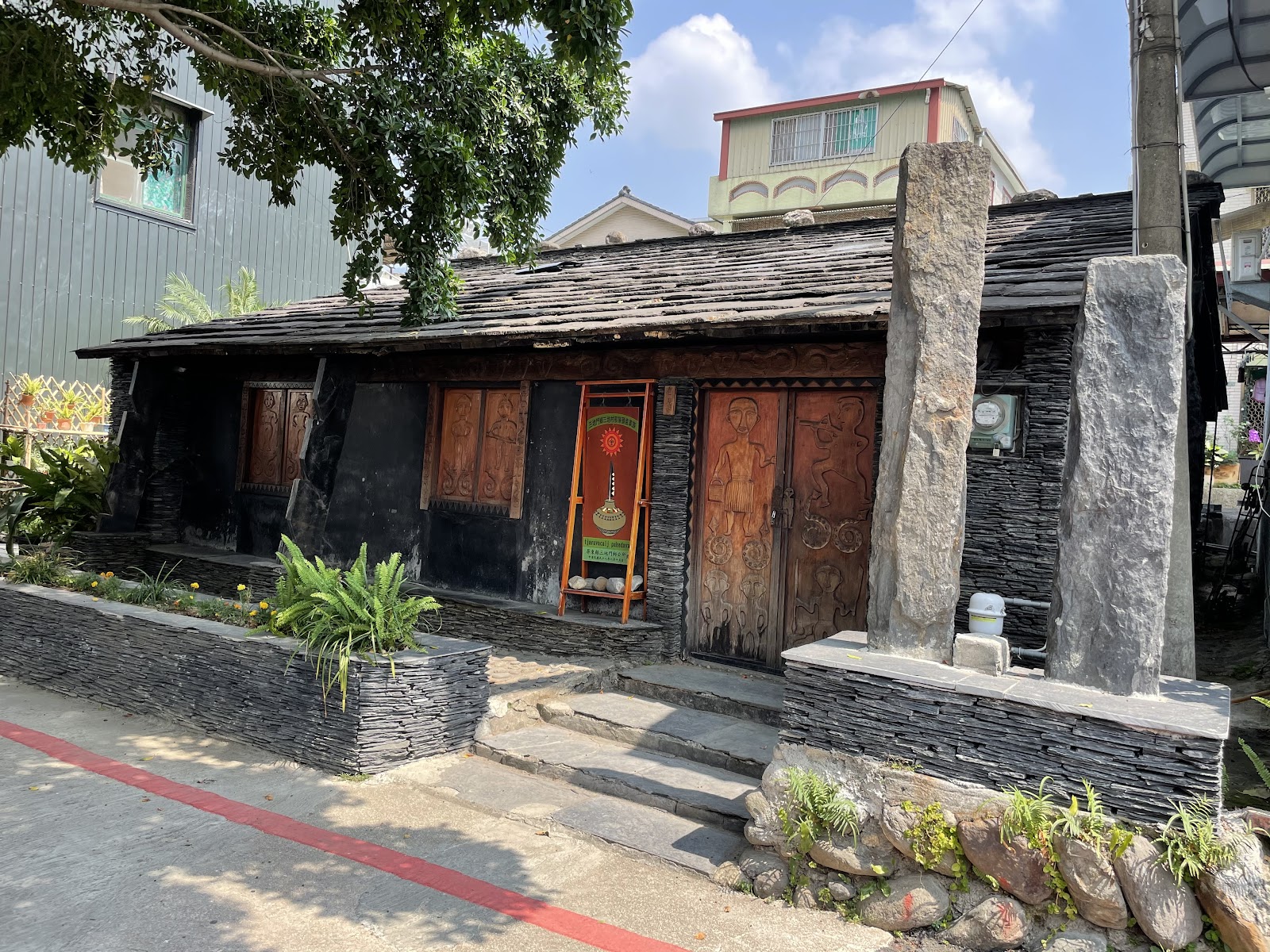 排灣族石板屋正面,深色石板牆配精緻木雕門板及石柱,屏東春日秘境
