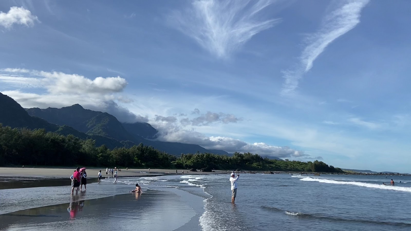 都歷黑沙灘，遊客戲水，背景是壯觀的海岸山脈和藍天白雲
