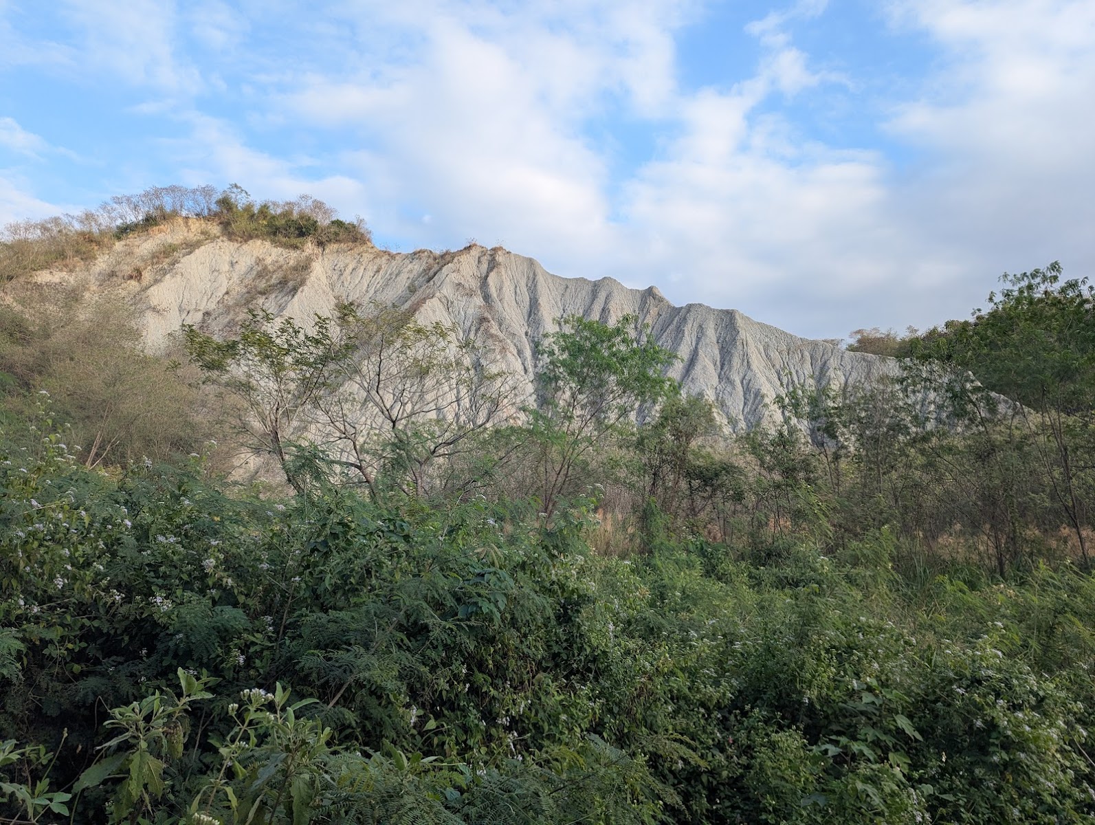 龍崎牛埔惡地泥岩山頭從綠樹叢中突出,白雲飄過天際